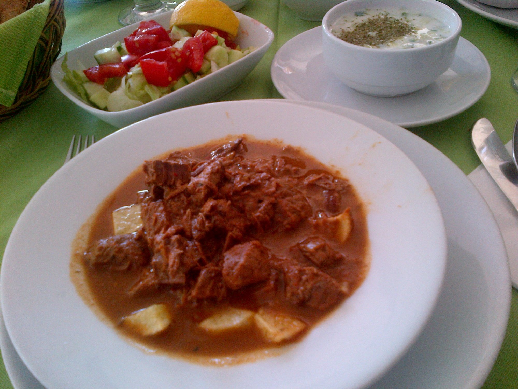 Patatesli tas kebabı; yanında çoban salatası ve cacık kâsesiyle servis
