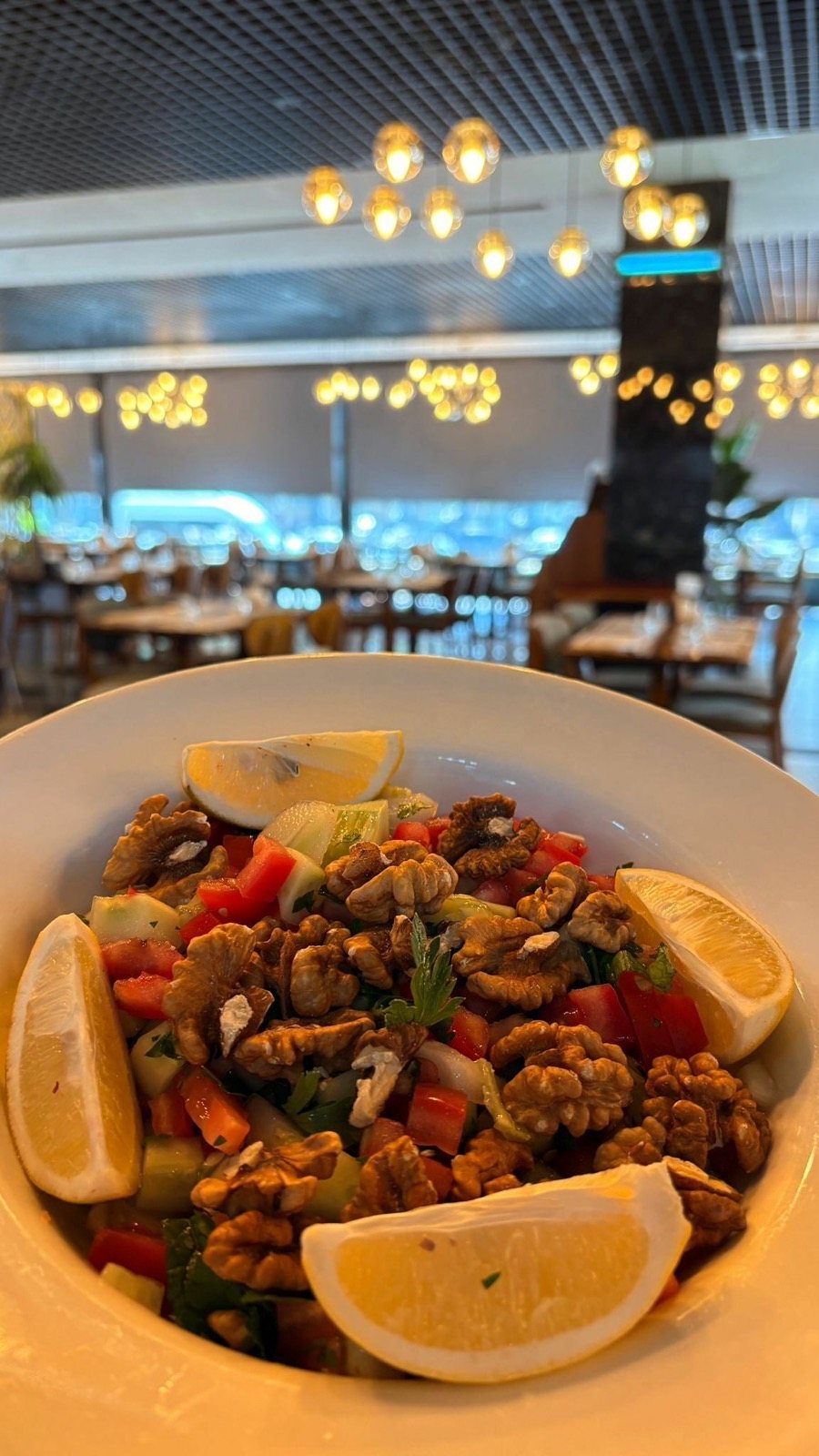 Beyaz kâsede cevizli gavurdağı salatası ve limon, arkada restoran salonu